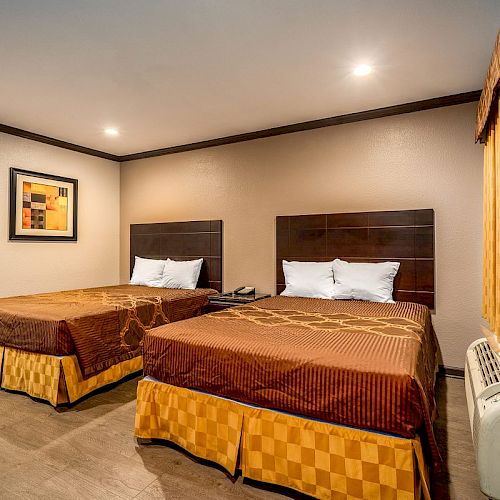 This image shows a hotel room with two double beds, brown and orange bedding, a wall painting, and warm lighting. The curtains match the bedding.