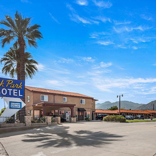 An outdoor view of Oak Park Motel, featuring a two-story building, palm trees, and a clear blue sky.