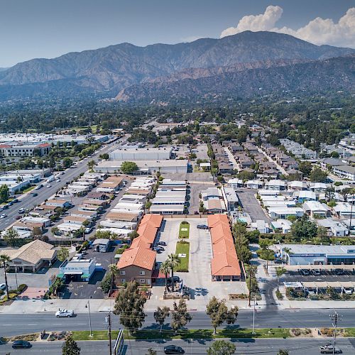 An aerial view of a suburban area with a mix of residential and commercial buildings, set against a backdrop of mountains and clear sky.