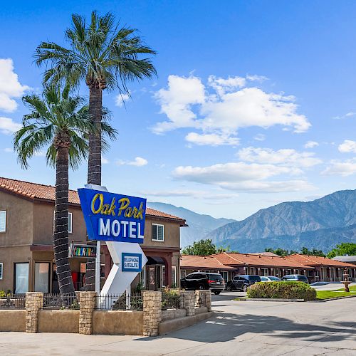 Image of the Oak Park Motel with palm trees, mountains in the background, and scattered clouds in the sky, suggesting a pleasant setting.