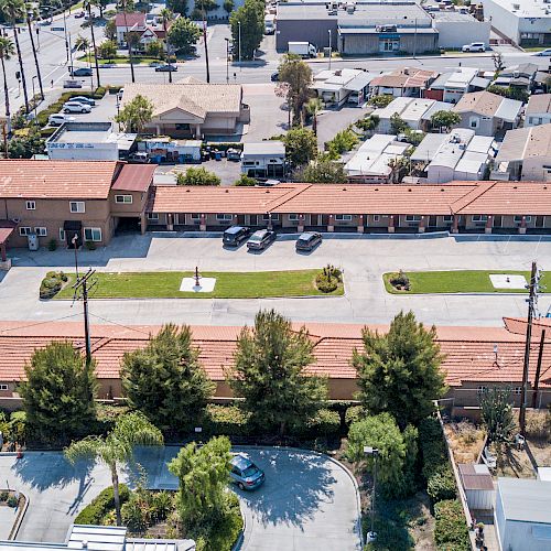 The image shows an aerial view of a compact neighborhood with buildings, roads, and parked cars, featuring a long building with a red roof.