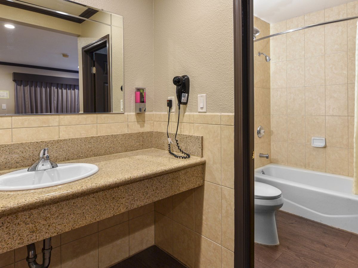 The image shows a bathroom with a sink and countertop, a mounted hairdryer, a mirror, and a bathtub with a shower curtain.