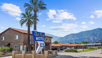 The image shows a motel with a sign reading "Oak Park MOTEL," palm trees, and mountains in the background under a blue sky with clouds.