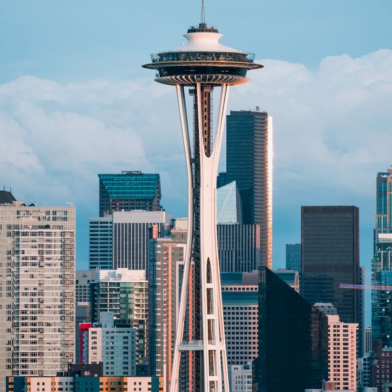 The image features the Space Needle in Seattle, with surrounding buildings and skyline under a partly cloudy sky.