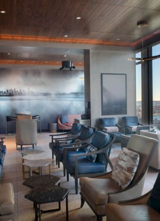 A modern lounge with comfortable seating, large windows offering a water view, and a cityscape mural on the back wall.